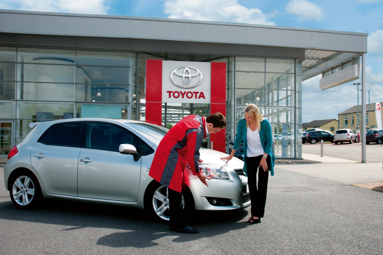 жена и техник на Toyota пред сервиза, които коментират предния фар на автомобила й