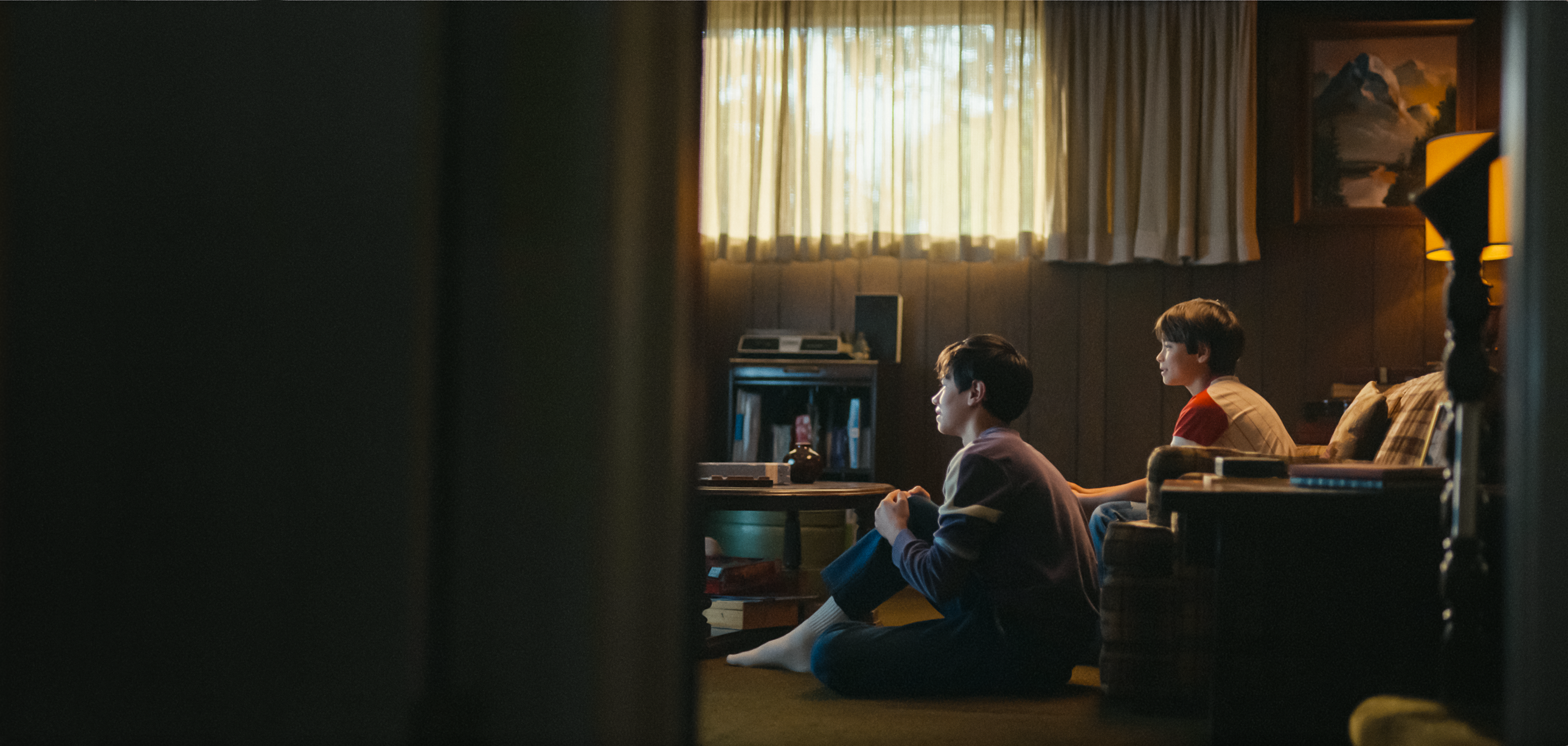 Ретроспективна снимка на двамата млади братя МакКийвър, които внимателно гледат телевизия у дома в хола си.