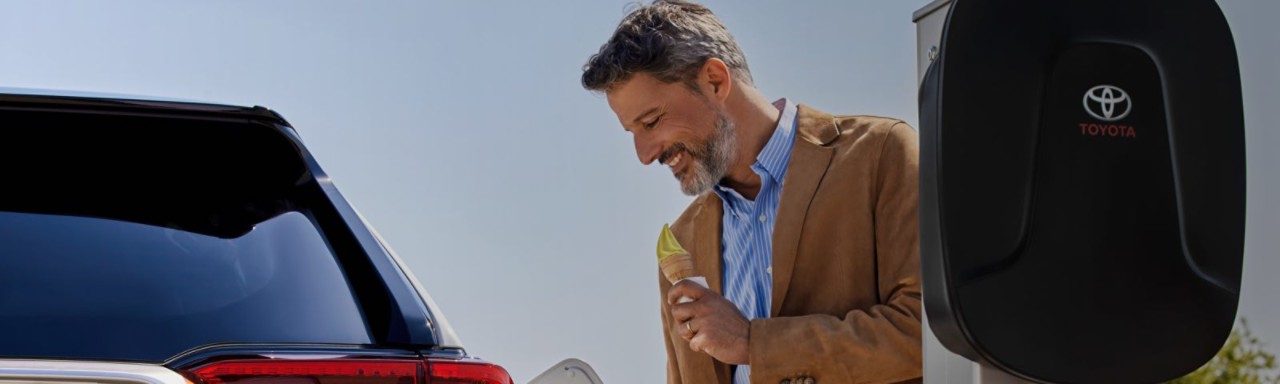 Щастлив мъж държащ сладолед зарежда електрически автомобил